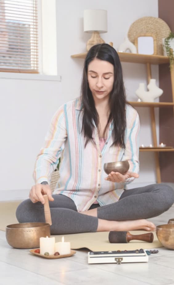 A healer sitting cross-legged among singing bowls and candles